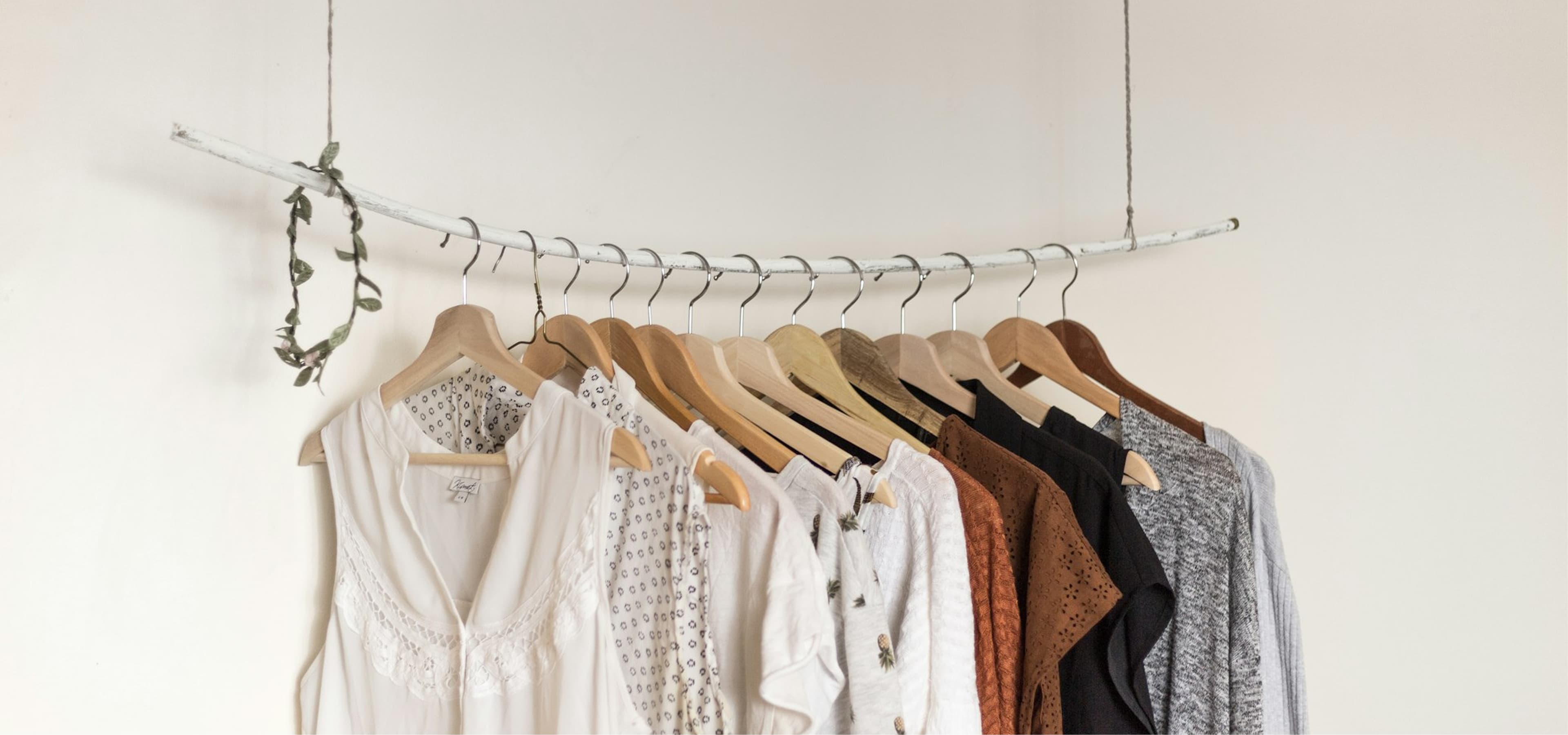 Curated neutral-toned garments on wooden hangers displayed along a rustic white branch